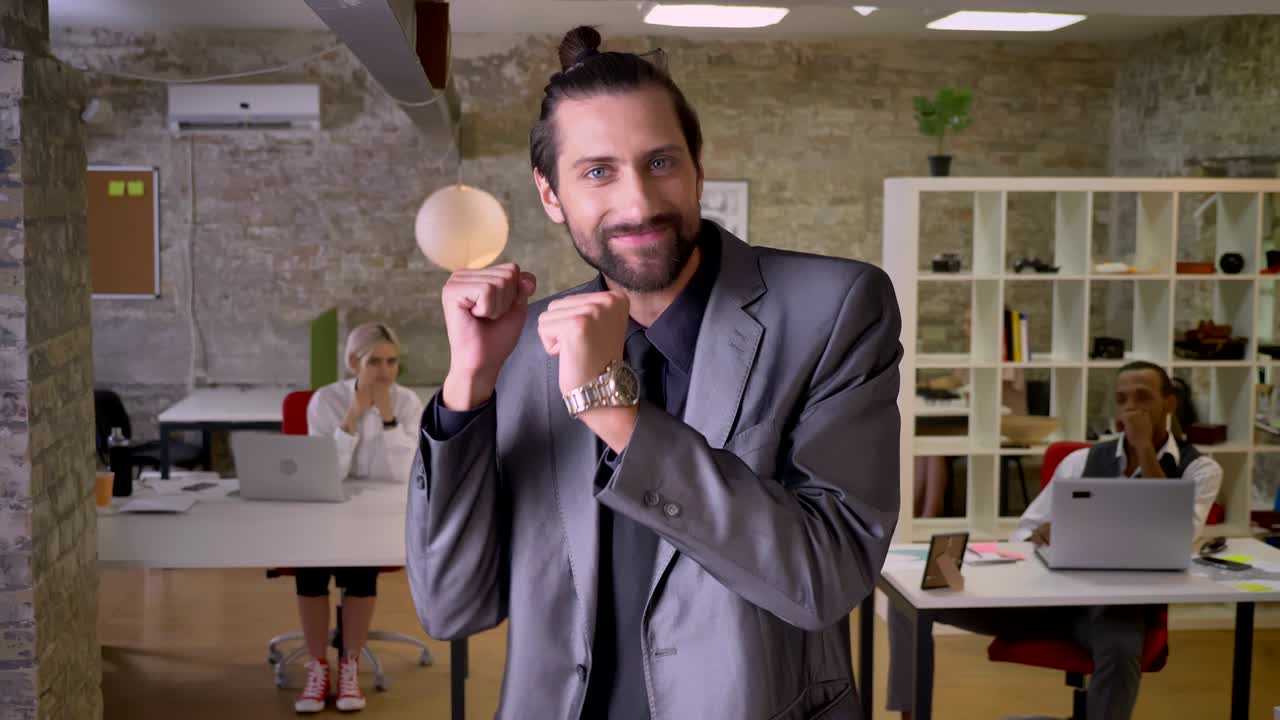 un hombre de negocios alegre con barba está bailando en la oficina, sonriendo, los colegas lo están mirando, concepto de trabajo, concepto de relajación