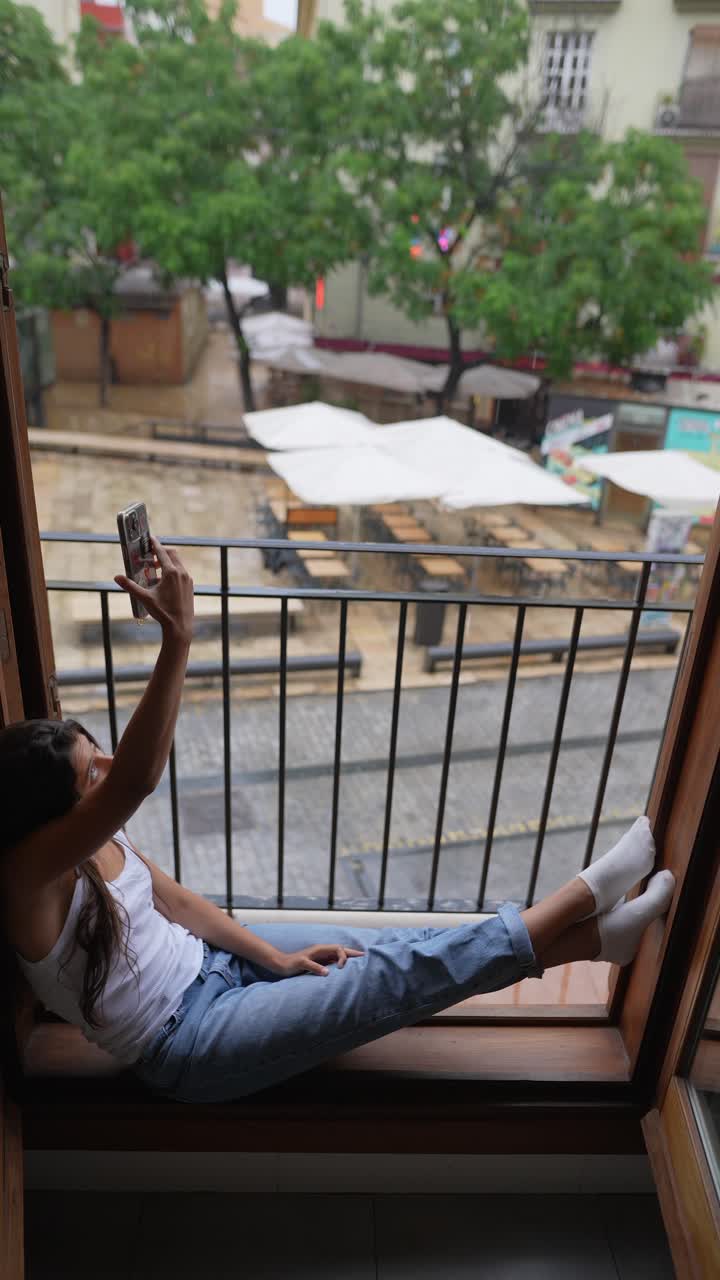 mujer tomando una selfie en el balcón durante un día de lluvia
