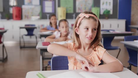 Happy-diverse-schoolgirls-at-desks-raising-hands-in-classroom-at-elementary-school