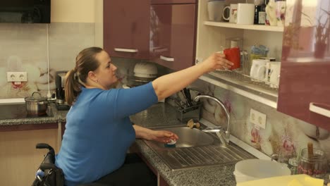 mujer con discapacidad en silla de ruedas lava platos en la cocina en el lavabo