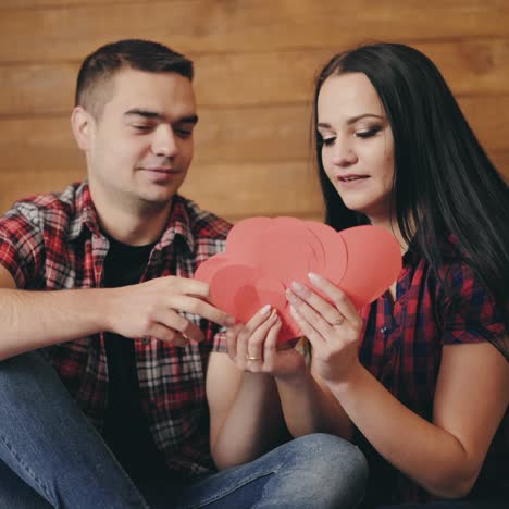 beautiful couple are laying out in their hands red paper hearts of large and small sizes on the background of a wooden wall in the studio. love story. valentine's day