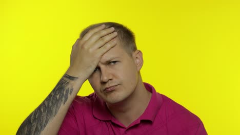 portrait of young caucasian man posing in pink t-shirt. dissatisfied guy puts hand on face, facepalm