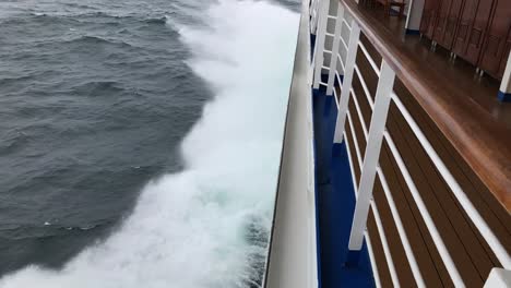 slow motion view of the spraying water off the left, port side of a ship as it hits the waves, lifting up, forward to the horizon