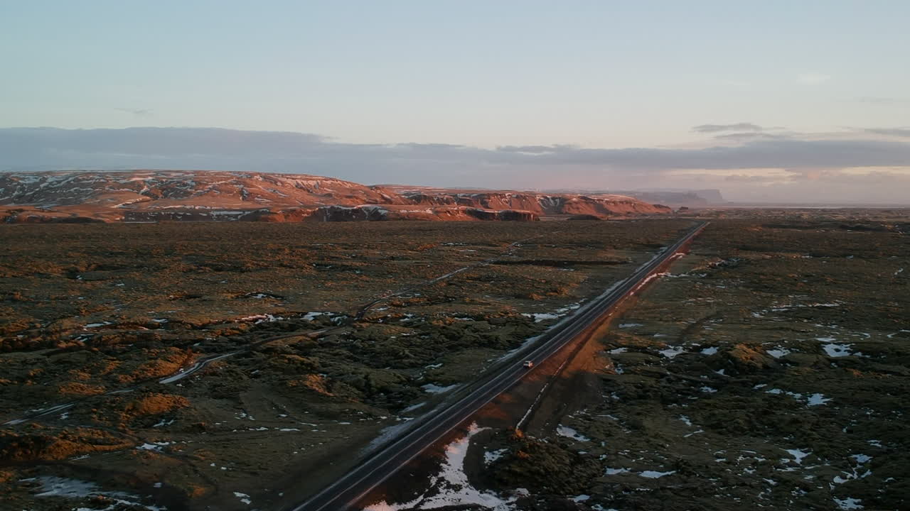 съемка с дрона с воздуха типичного пейзажа исландии с проезжающим автомобилем, красным песком, красными горами и снегом