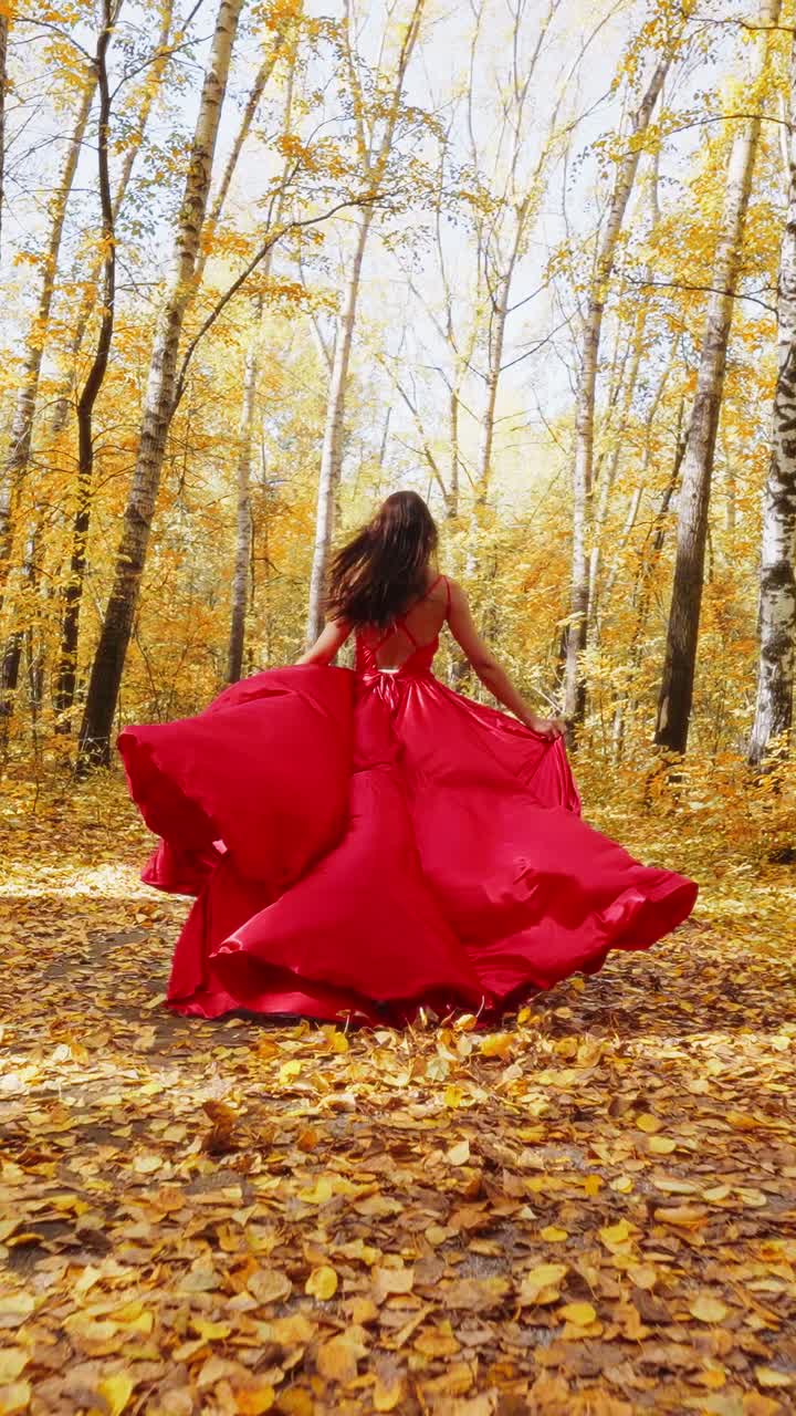A Stunning Model in a Flowing Red Dress Gracefully Walking Through a Beautiful Autumn Forest, Surrounded by Golden Leaves and Glowing Trees