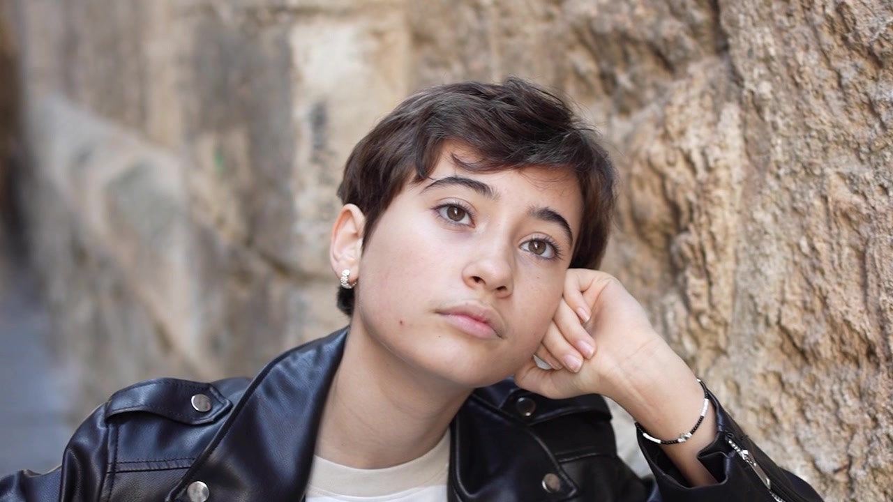 Una persona giovane e pensierosa è immersa nella contemplazione mentre è seduta in un ambiente urbano.