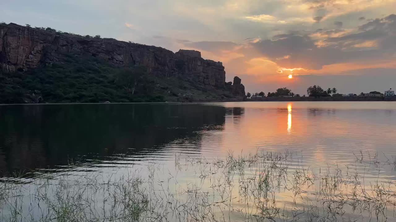 Um time-lapse em câmera lenta das nuvens do pôr do sol e das águas do lago, com as impressionantes cavernas de arenito vermelho de Badami à vista