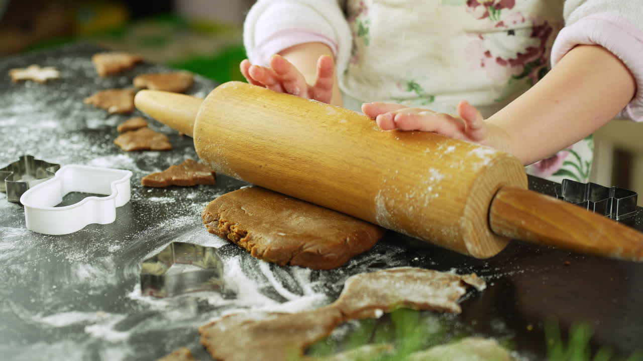 Baking gingerbread cookies with a rolling pin, child hands shaping festive dough