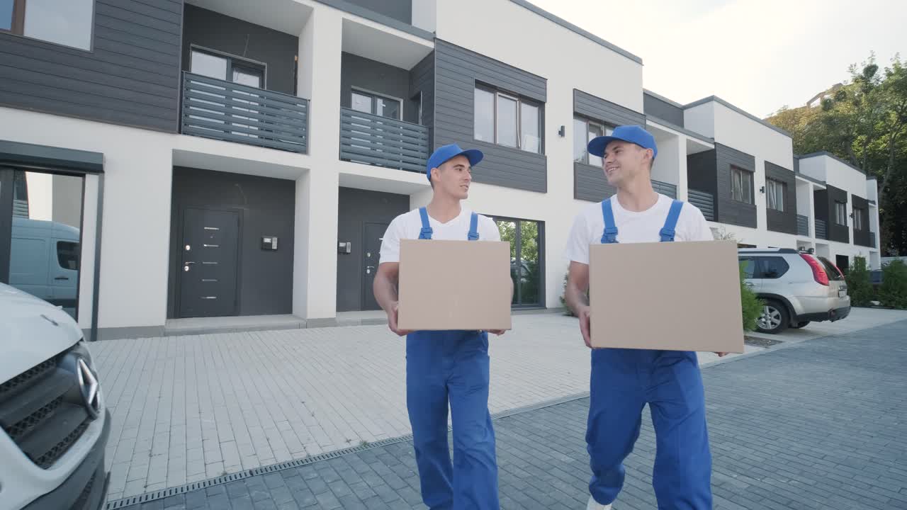 Two young workers of removal company are loading boxes and furniture into a minibus