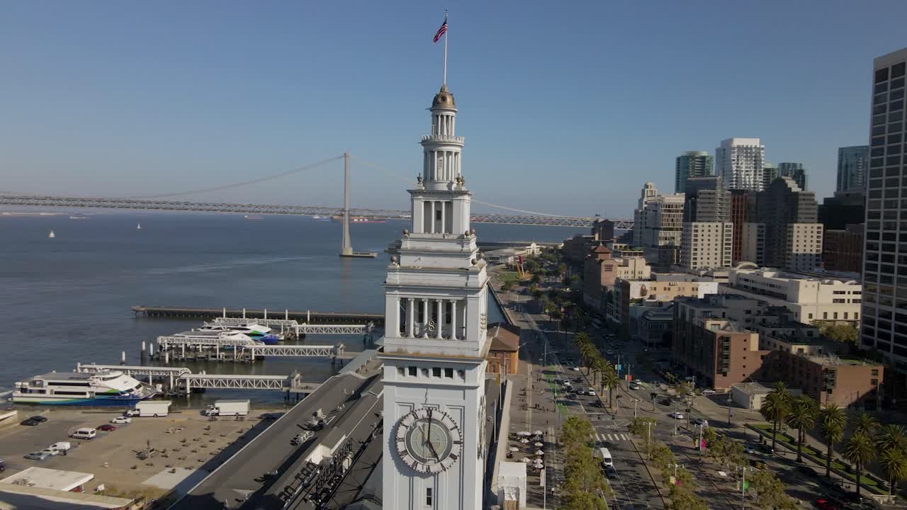 This dynamic drone footage orbits around San Francisco's iconic Ferry Building, providing a stunning panorama of the Bay Bridge and the city's towering downtown buildings