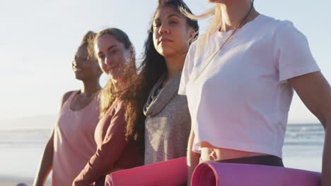 group of diverse female friends holding yoga mats at the beach