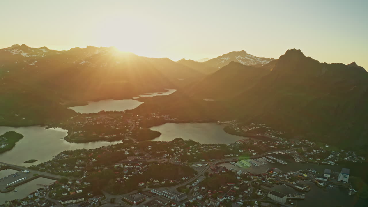 Aerial drone shot over the Norwegian town of Svolvaer in the Lofoten Islands, Norway. Bird's eye view of the fishermen's town at the midnight sun. View of the vast mountains in the background.