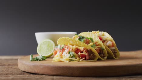 Video-of-freshly-prepared-tacos-and-bowl-with-sauce-lying-on-board-on-grey-background