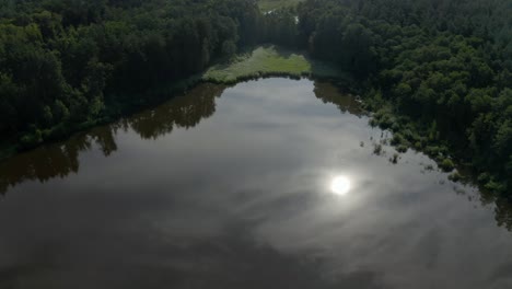 Ucrania---Hermoso-Lago-Que-Refleja-El-Sol-Y-Las-Nubes-Del-Cielo,-Rodeado-De-árboles-Altos---Imágenes-De-Drones