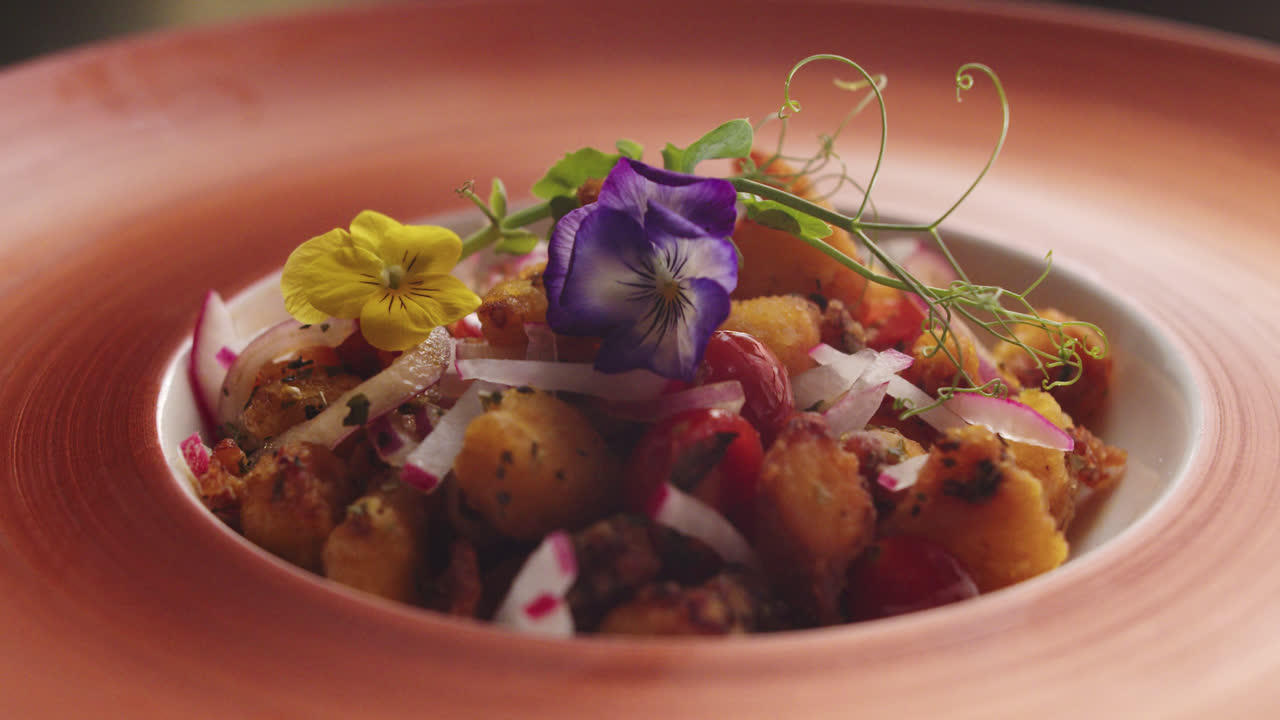 Chef che impiattano un piatto gourmet con fiori commestibili.