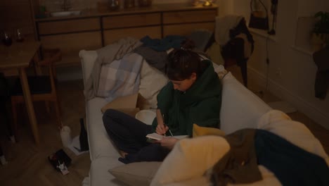 woman writing on couch in messy home