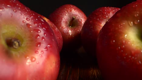 primer plano de frutas de manzana rojas con gotas de agua en una mesa de madera sobre un fondo negro