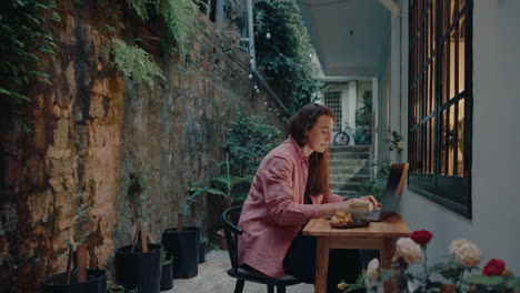 young woman bringing tea and pastry, working on laptop outside the house