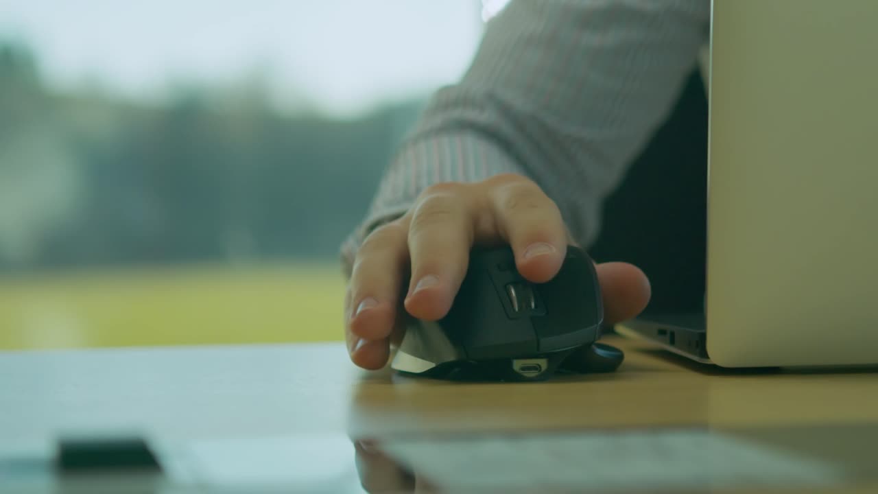 Caucasian male moving wireless mouse next to laptop on desk, slow motion
