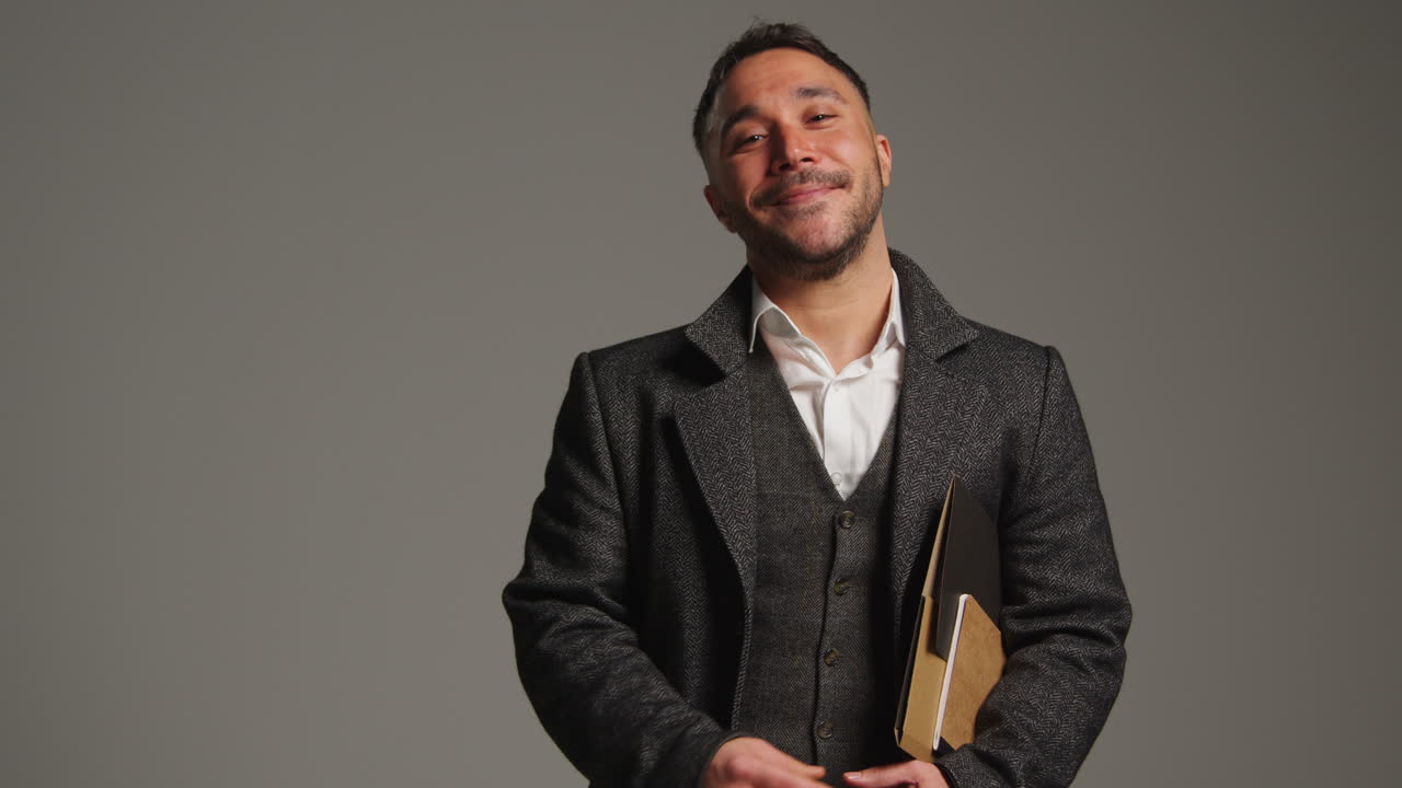 retrato de estudio de un maestro o hombre de negocios maduro sonriente de pie contra un fondo gris con una carpeta bajo el brazo