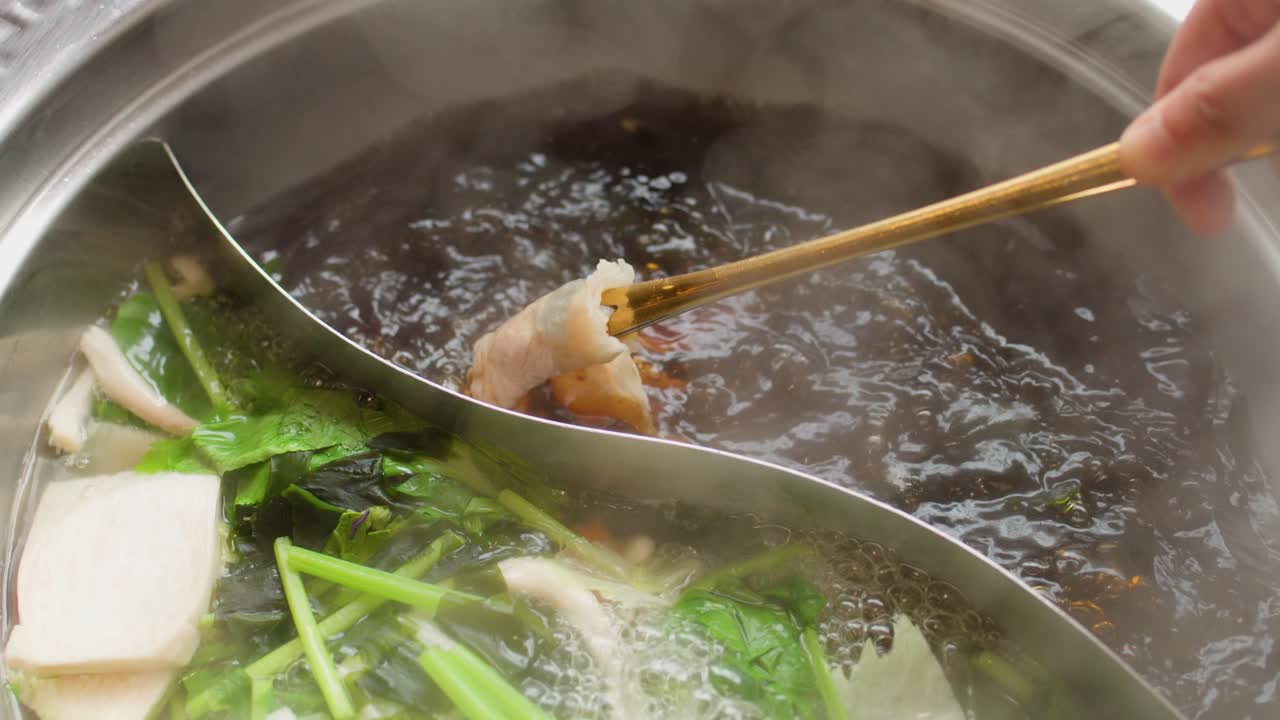 Thinly sliced meat cooks in steaming dual broth hotpot with fresh vegetables, overhead close-up