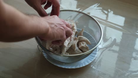 separating boiled chicken meat by hand over plate – overhead close-up shot