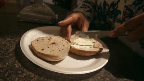 Schwarze-Junge-Frau,-Die-Zum-Frühstück-Frischkäse-Auf-Einen-Bagel-Schmiert