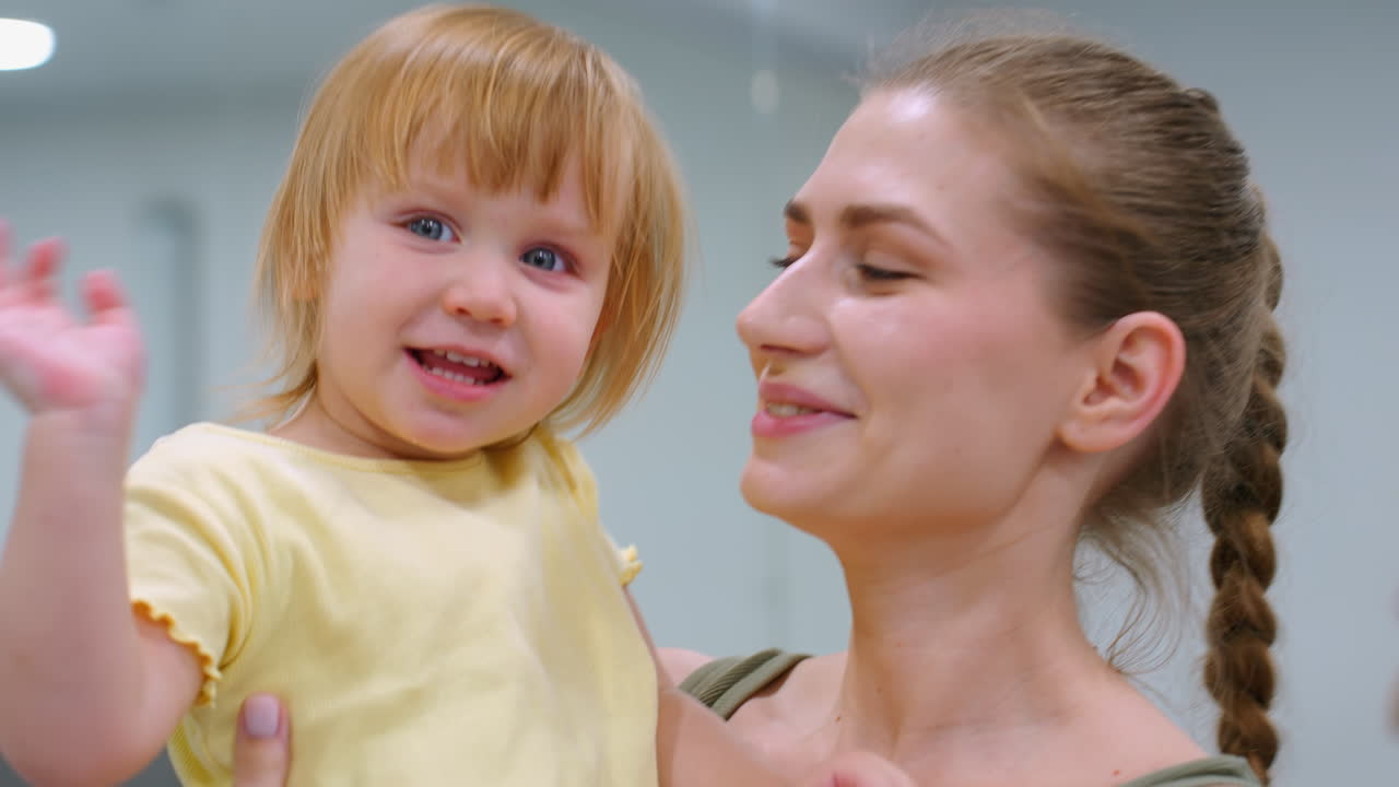 primer plano de la unión de la madre y el niño mientras el niño se despide juguetón, sonrisas cálidas y afecto entre ellos, el espejo en el fondo refleja a alguien borroso