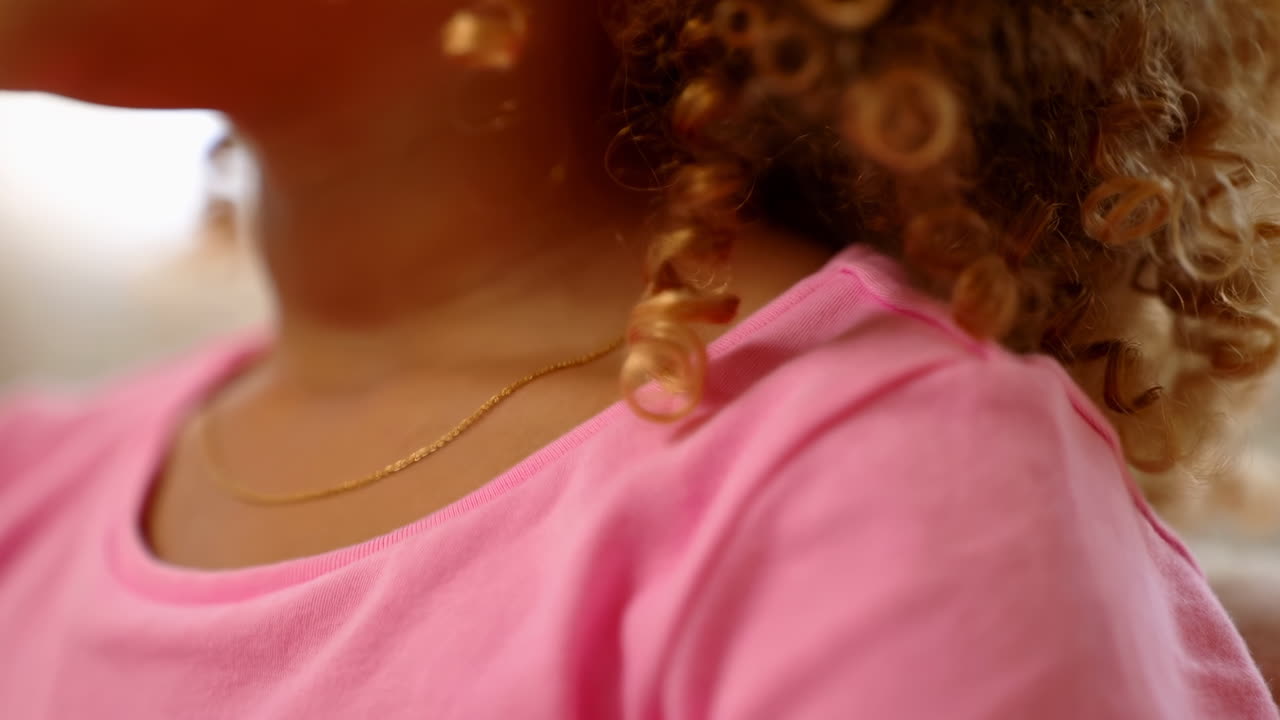 Ritratto ravvicinato di un bambino con capelli ricci, luce solare morbida e calda, maglietta rosa e collana delicata, profilo spontaneo.