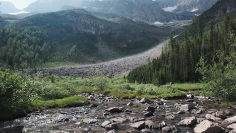 a rugged rocky scree slope descends to a crystal-clear stream fed by melting glacier waters