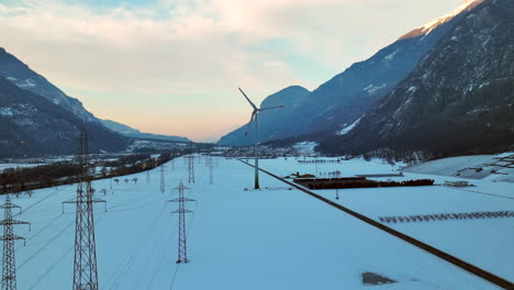 Largas-Líneas-Eléctricas-Junto-A-Un-Moderno-Molino-De-Viento-Giratorio-En-El-Valle-Del-Ródano-En-Una-Noche-De-Invierno