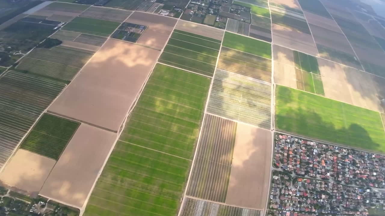Vast cityscape with farmlands divided into rectangular fields in the middle. Landscape from FPV drone footage among the clouds.