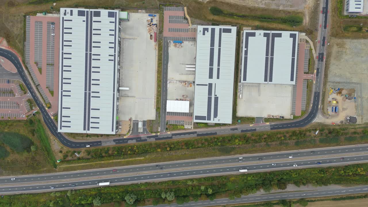Top down aerial drone shot of Bedfordshire UK motorway traffic with nearby industrial distribution centres, factory warehouses and logistics facilities