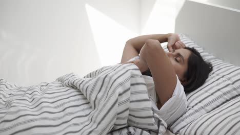 a young woman lies in a bed, then she removes the blanket and gets up