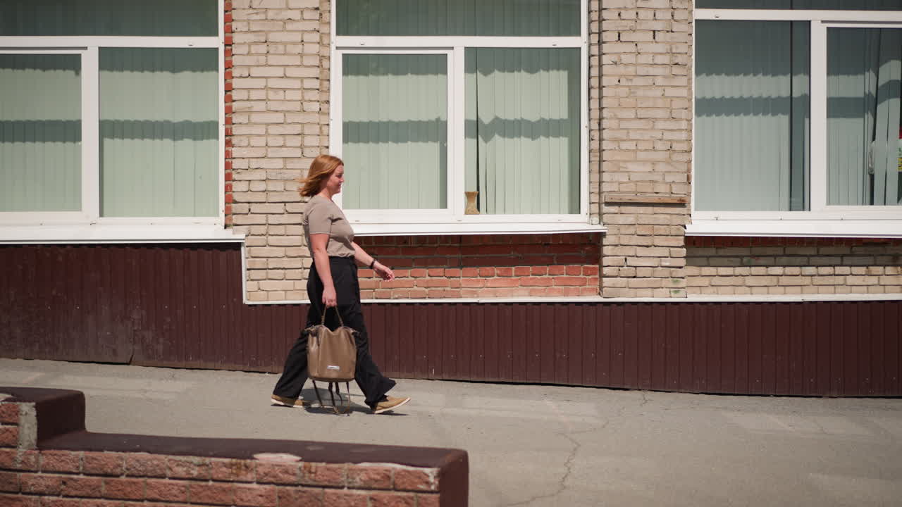 Student walking out of classroom holding brown bag under bright sunlight, expression calm and thoughtful, brick school building and open door reflecting peaceful daily life