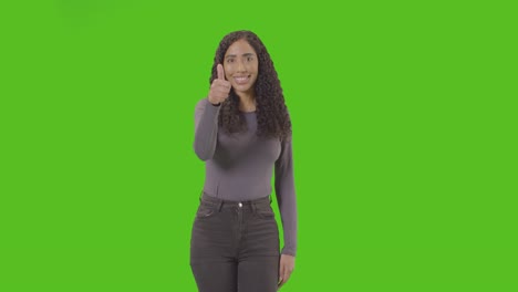 studio three quarter length shot of woman giving thumbs up sign against green screen