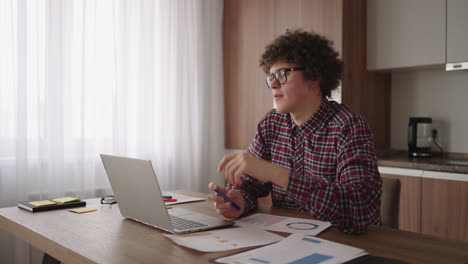 brooding serious curly freelancer man sit at table in comfortable home office room work on laptop looks concentrated thinking over business issue solution makes telecommute job