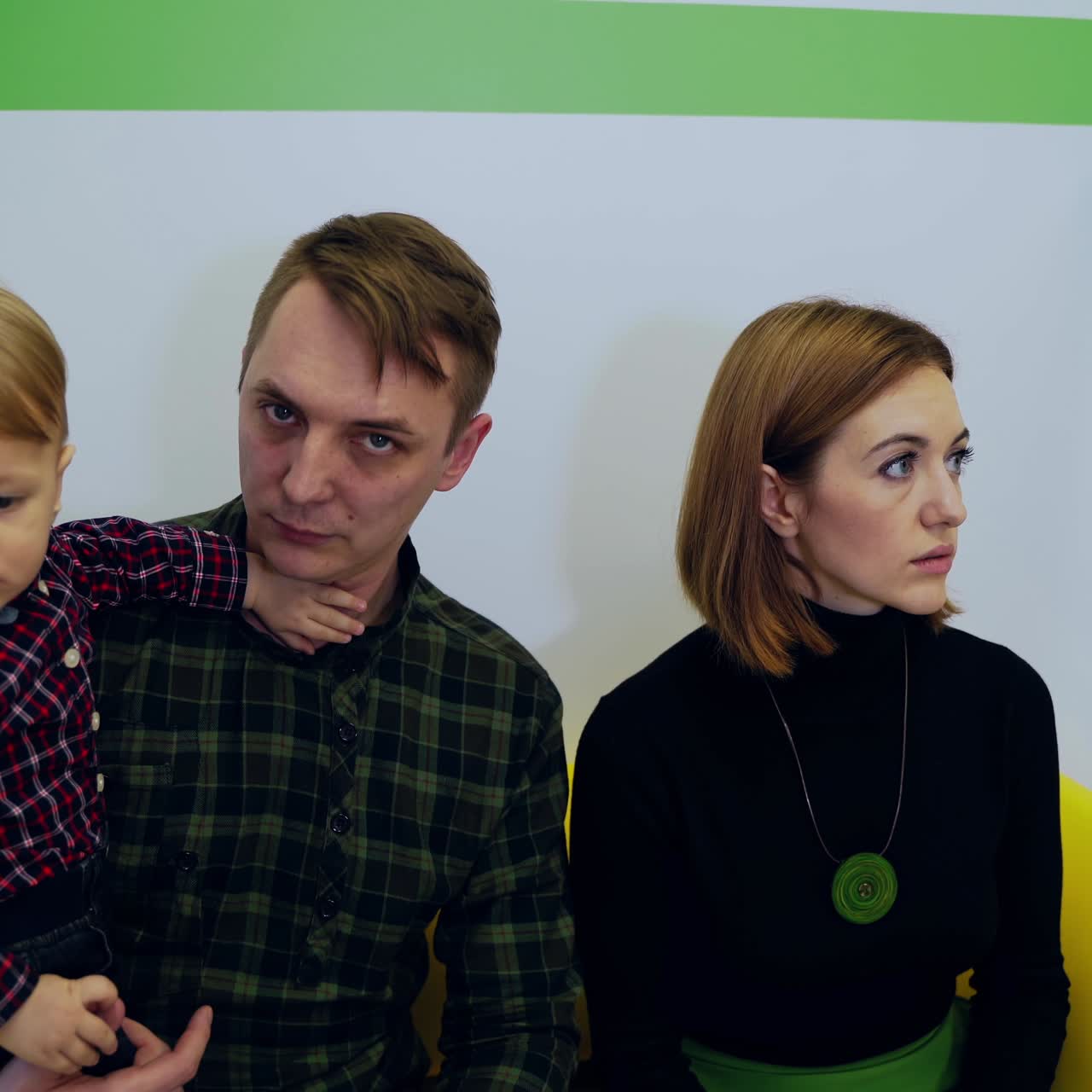 Man pediatrician and parents with child. Cute kid boy in father's hands at medical consultation. Young parents sitting on couch with child and talk to doctor.