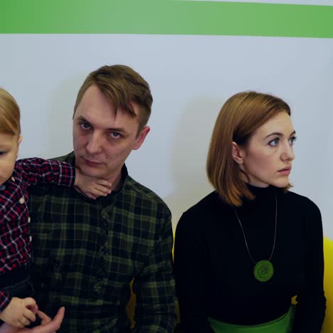 man pediatrician and parents with child. cute kid boy in father's hands at medical consultation. young parents sitting on couch with child and talk to doctor.