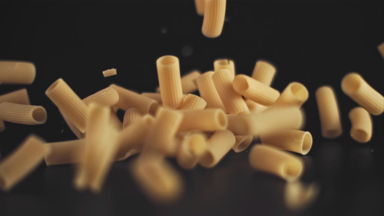 Pasta maccheroni secca che cade al rallentatore su sfondo nero.