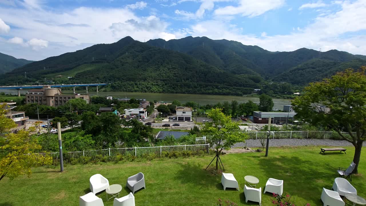 Camera pans left from a terraced hillside cafe to reveal a beautiful panoramic view of the Bukhangang River and Hwayasan Mountain in Gapyeong, South Korea, cars traffic at mountain base