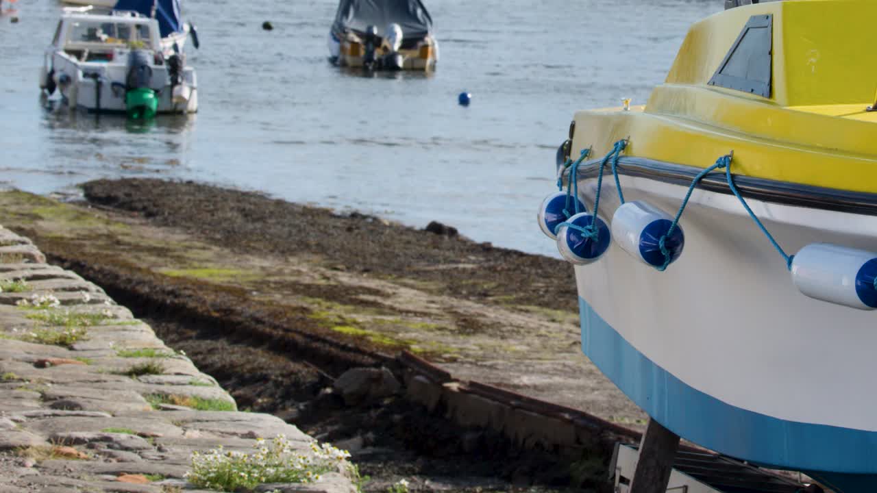 Stationary camera captures colorful boats moored in calm harbor, natural daylight, stone slipway foreground