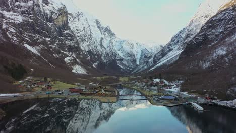 spectacular gudvangen village by unesco naeroyfjord during cold winter morning - downward moving aerial above fjord while looking at gudvangen village with mountain background and reflections in fjord