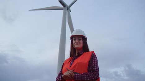 Frau-Ingenieur-Techniker-Lächelt,-Blick-In-Die-Kamera-Mit-Windkraftanlage-Dahinter