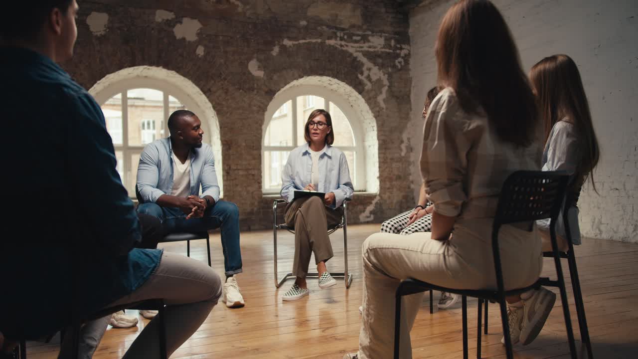 A girl psychologist in glasses with a bob haircut completes group therapy and its participants get up from their seats and leave. Completing Group Therapy