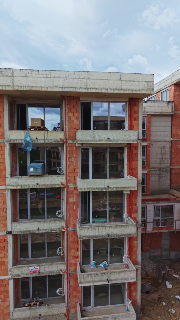 Processo de construção de um edifício de vários andares em uma área urbana com paredes de tijolo e caixilhos de janela visíveis durante o dia.