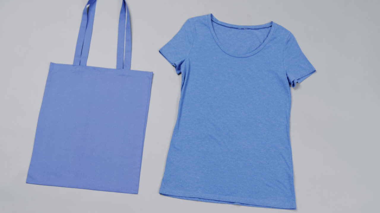 Primo piano di borsa blu e maglietta su sfondo grigio, con spazio per il testo, al rallentatore.