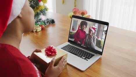 Afroamerikanische-Frau-Mit-Weihnachtsmütze-Nutzt-Laptop-Für-Weihnachtsvideoanruf-Mit-Der-Familie-Auf-Dem-Bildschirm