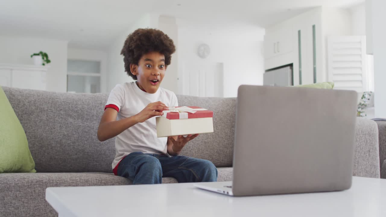 joven abriendo una caja de regalos mientras tiene chat de video en su computadora portátil