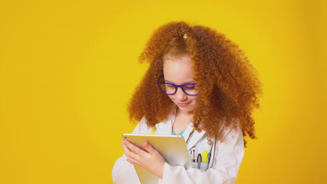 studio portrait of girl dressed as doctor or surgeon with digital tablet against yellow background